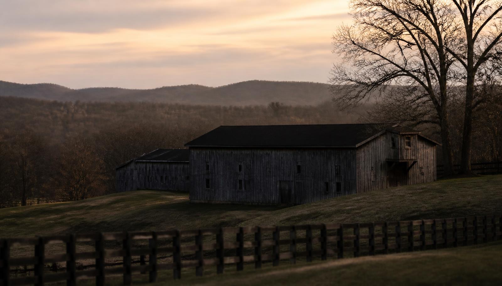 A weathered rickhouse in rolling American whiskey country at dusk